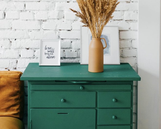 A rustic green wooden dresser table styled with a dry grass floral arrangement vase and white picture frames